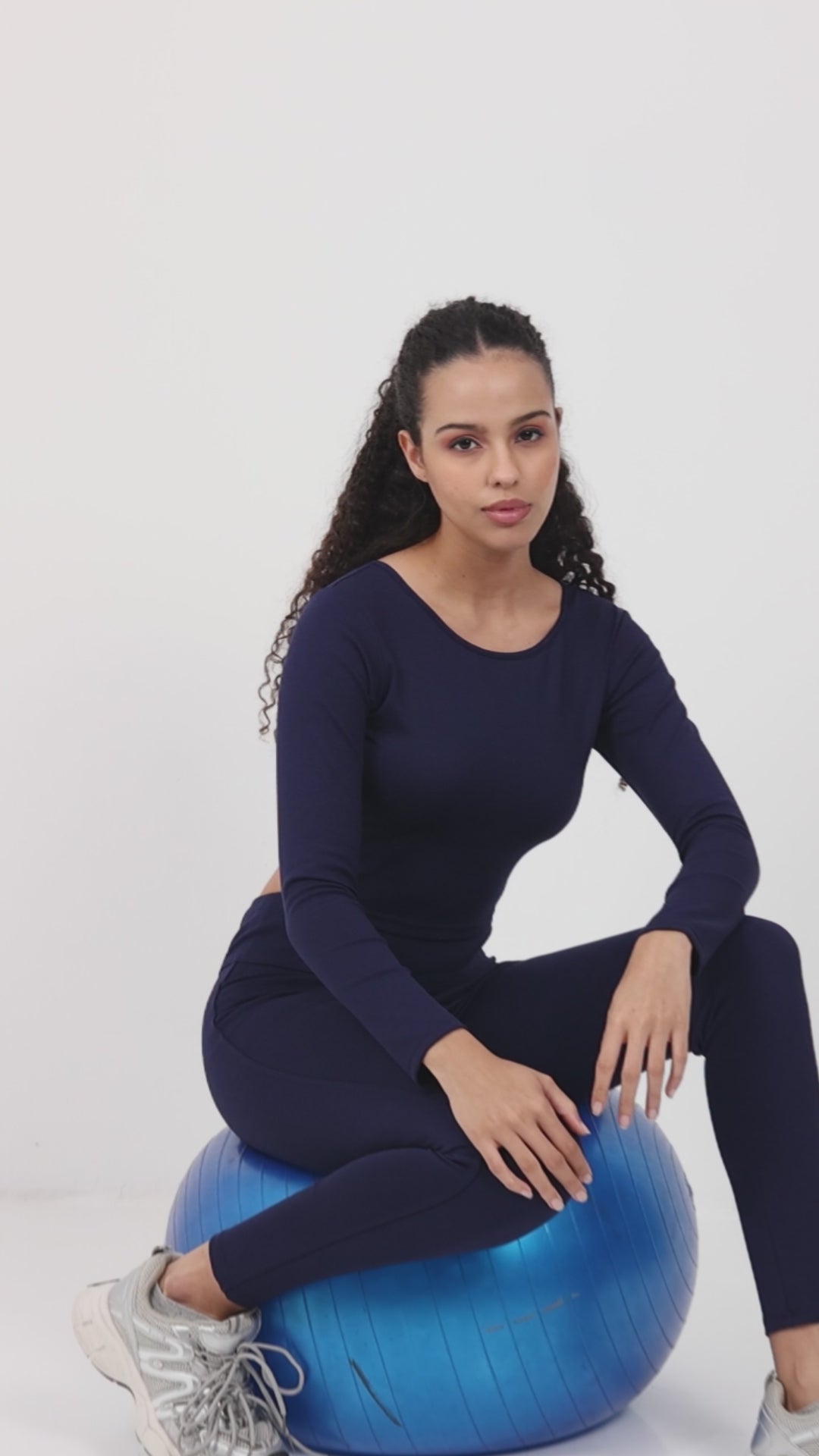 Model in navy Yellowcrop long sleeve crop top and matching leggings seated on exercise ball